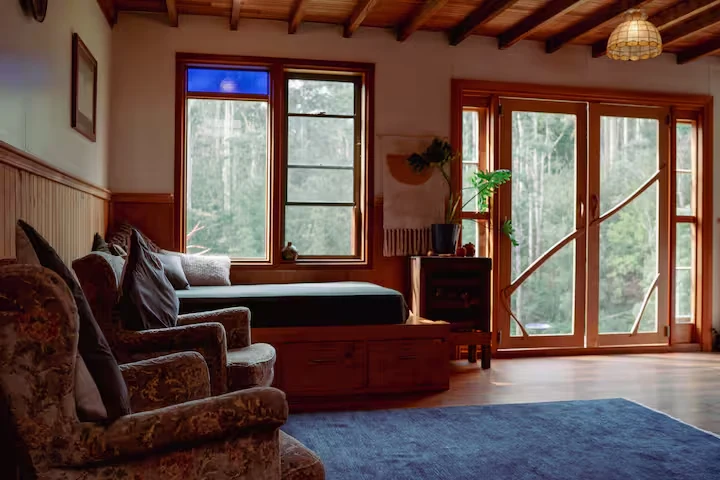 Timber-lined living room with vintage chairs and forest-facing doors